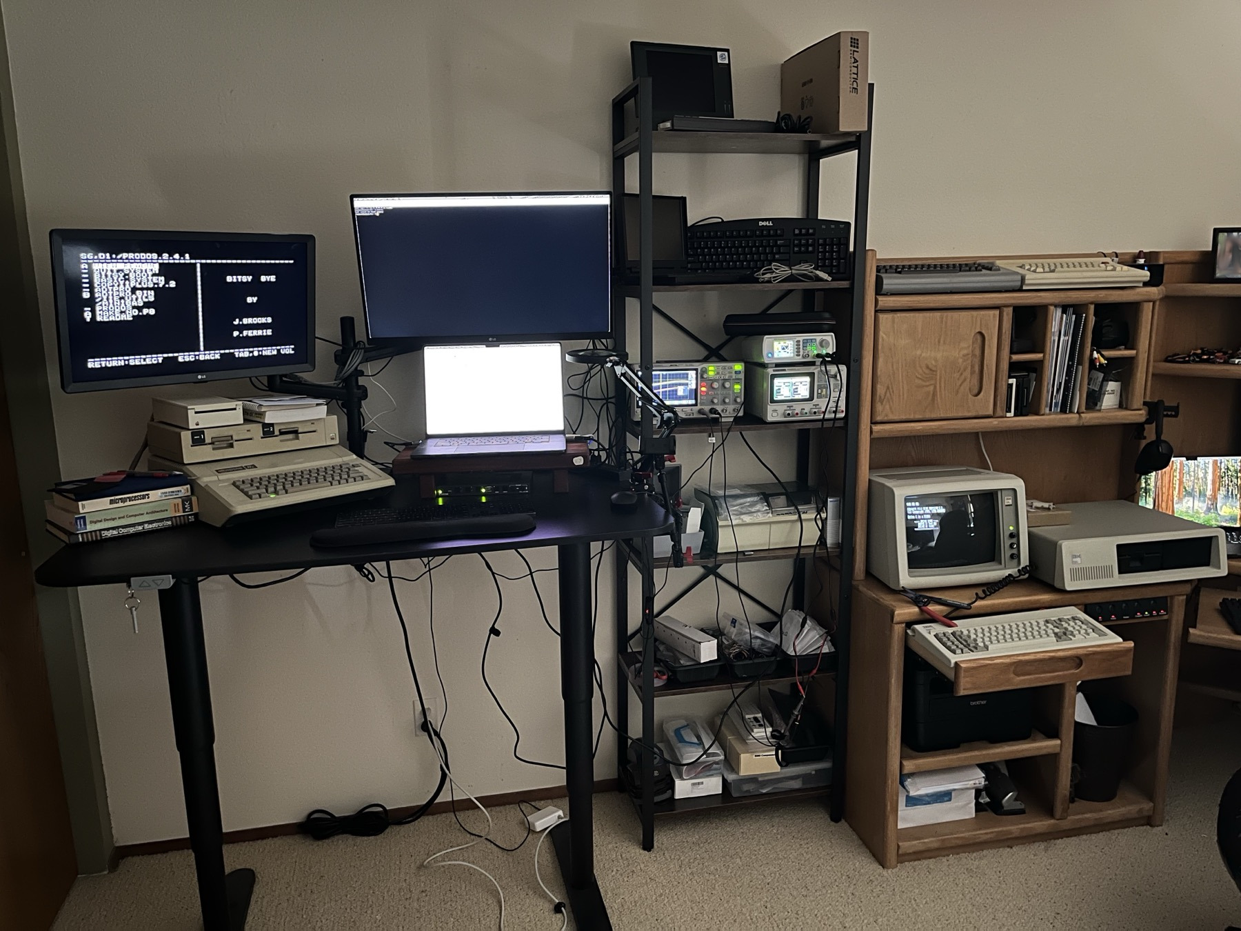 The lab: Apple IIe with disk drives on a standing desk, laptop and monitor, shelf of test gear, IBM PC on the desk next to it