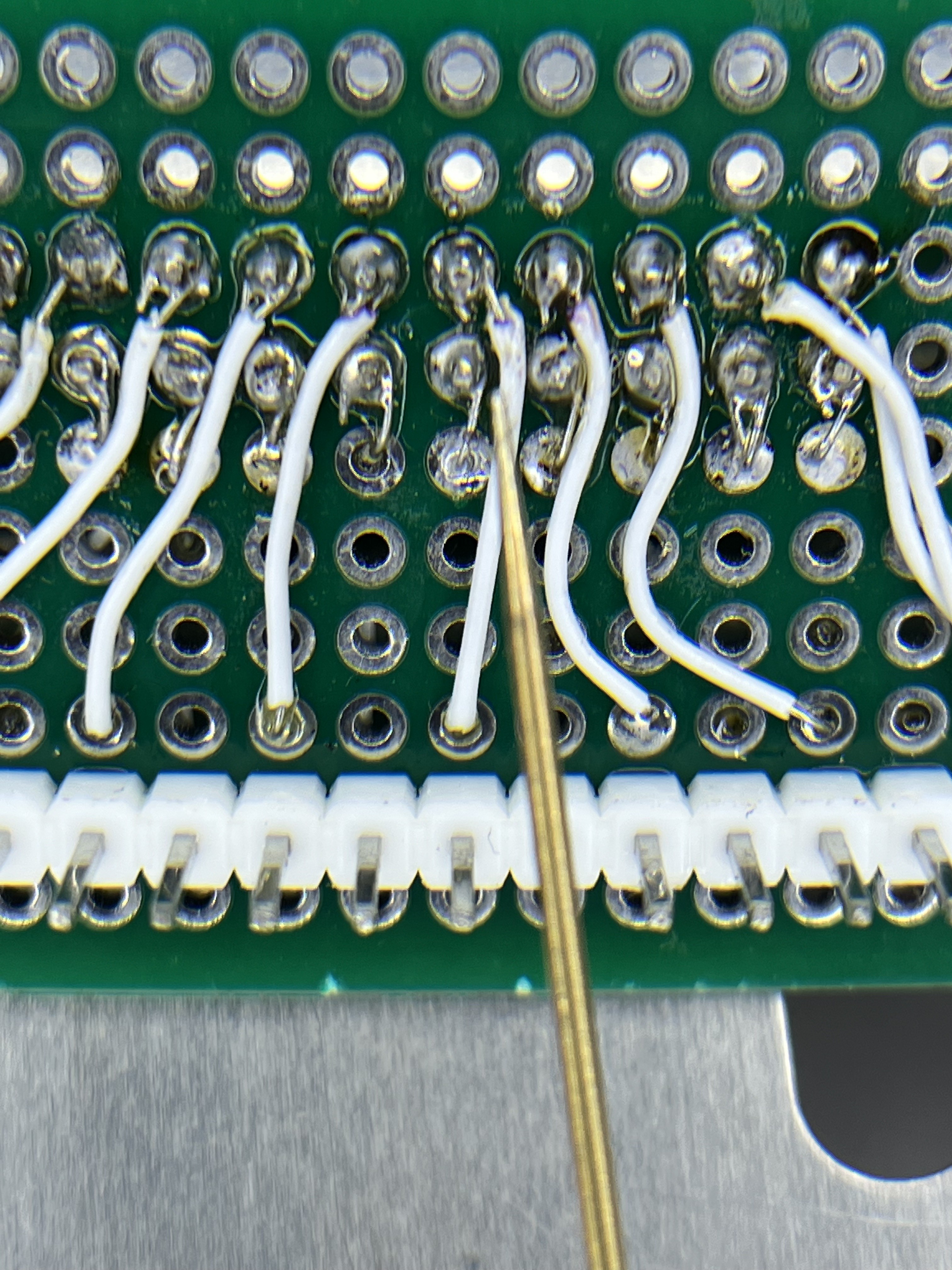 The homemade DB-19 adapter. The tweezers point at a loose strand from one wire reaching the next pad: strip position 9 (-12 V) to position 10 (/WRREQ).